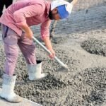 Worker in a pink shirt spreading concrete on a construction site with a shovel.