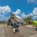 Construction workers laying concrete for a driveway in Fort Worth, Texas, under a bright blue sky.